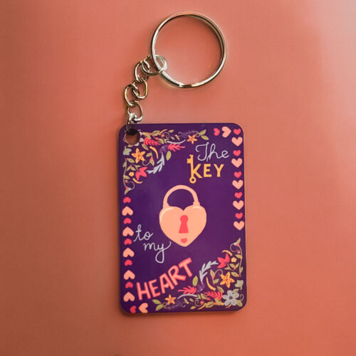 A deep purple design featuring a pink heart-shaped padlock and the text "The KEY to my HEART," decorated with colorful flowers and pink hearts.
